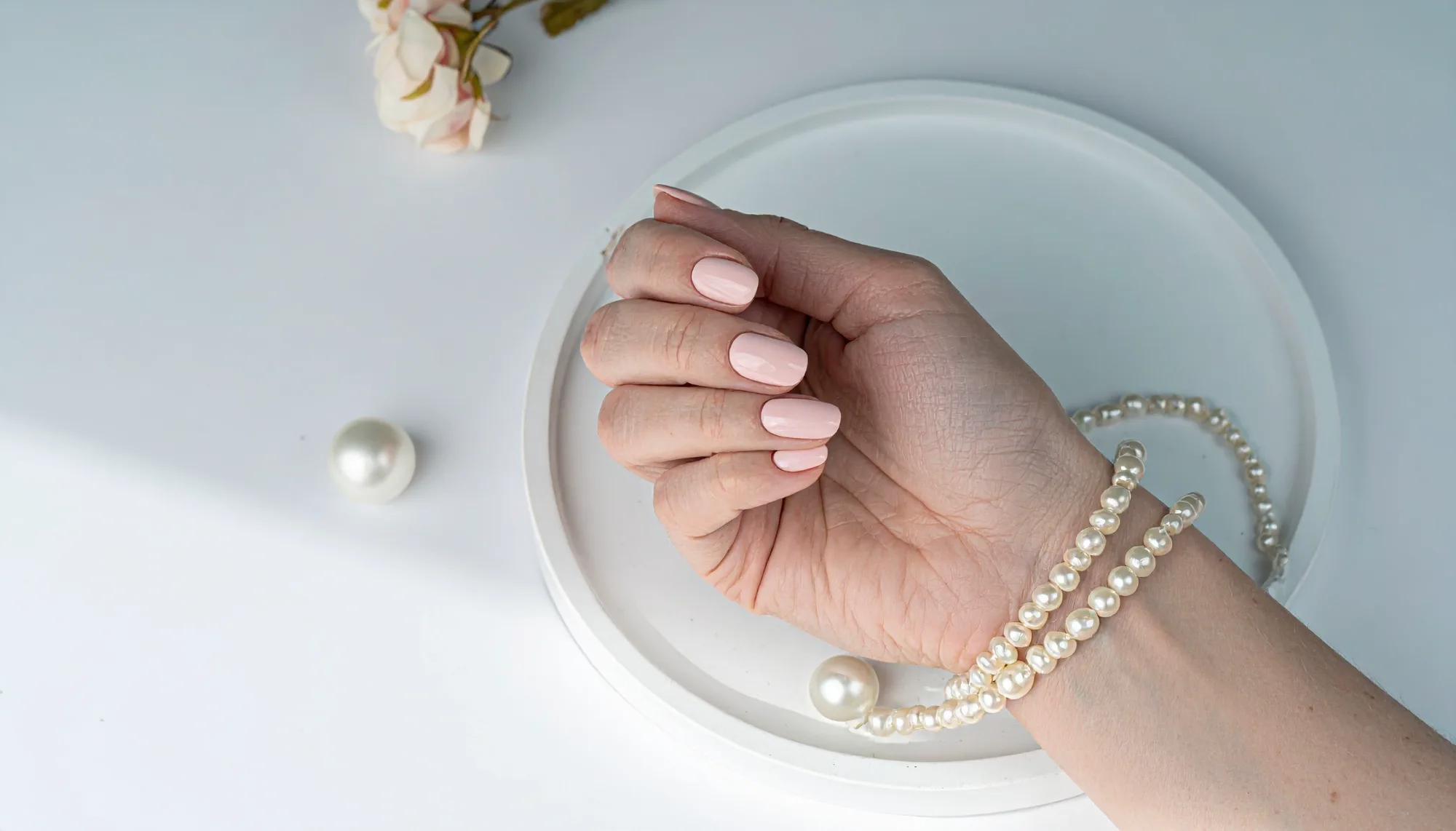 Soft pink manicure photographed with pearl styling on a cream tray
